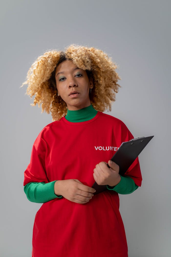 services-03 Young volunteer woman with curly hair holding a clipboard in a studio setting.